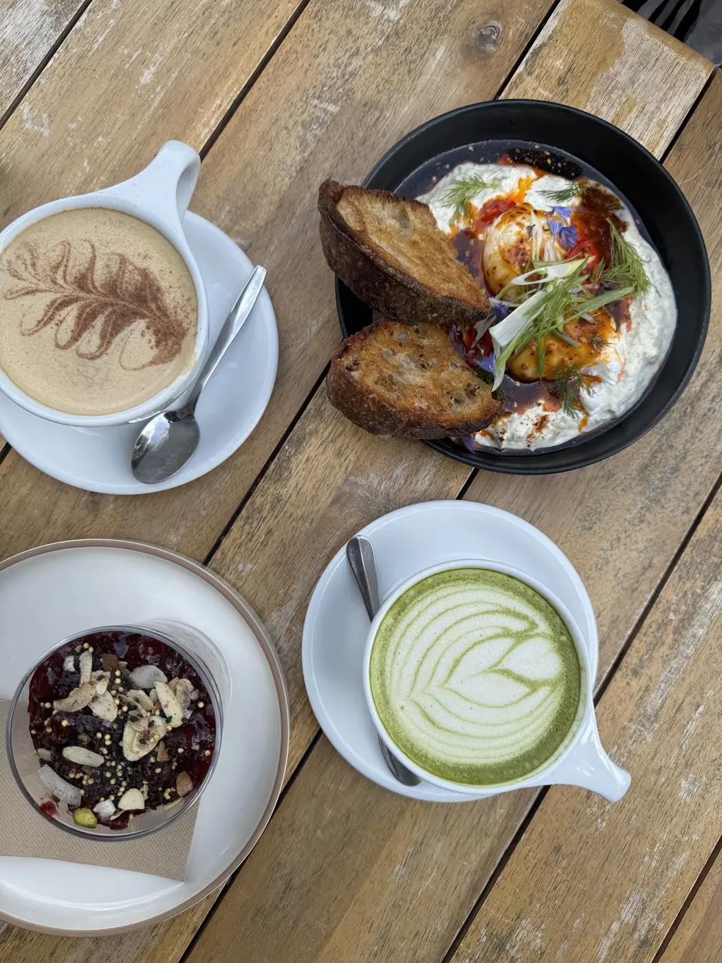 Turkish eggs with sourdough toast, a matcha latte, a cortado and a berry pot on a sunlit outdoor table